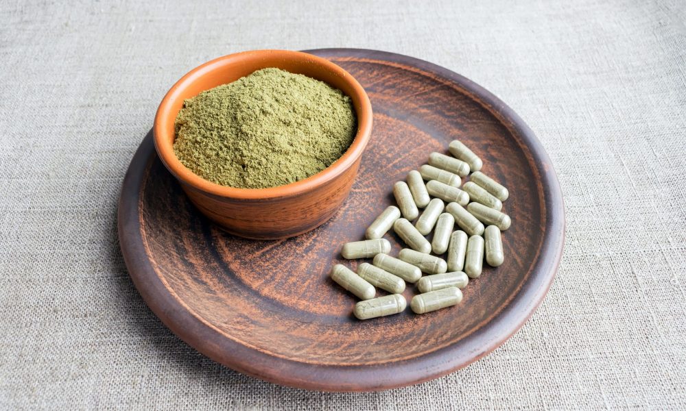 Supplement kratom green capsules and powder on brown plate. Herbal product alt-medicine kratom is  opioid. Home alternative pain remedy, opioid addiction, dangerous painkiller, overdose. Close up