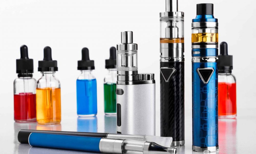 Modern electronic cigarettes and bottles with assorted vape liquid on white background